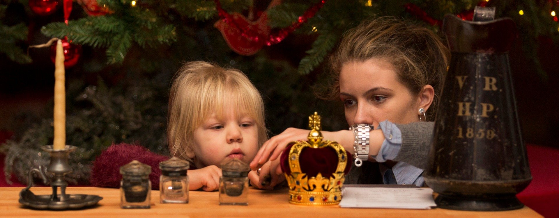 A woman and a child look at objects on a table in front of Christmas decorations