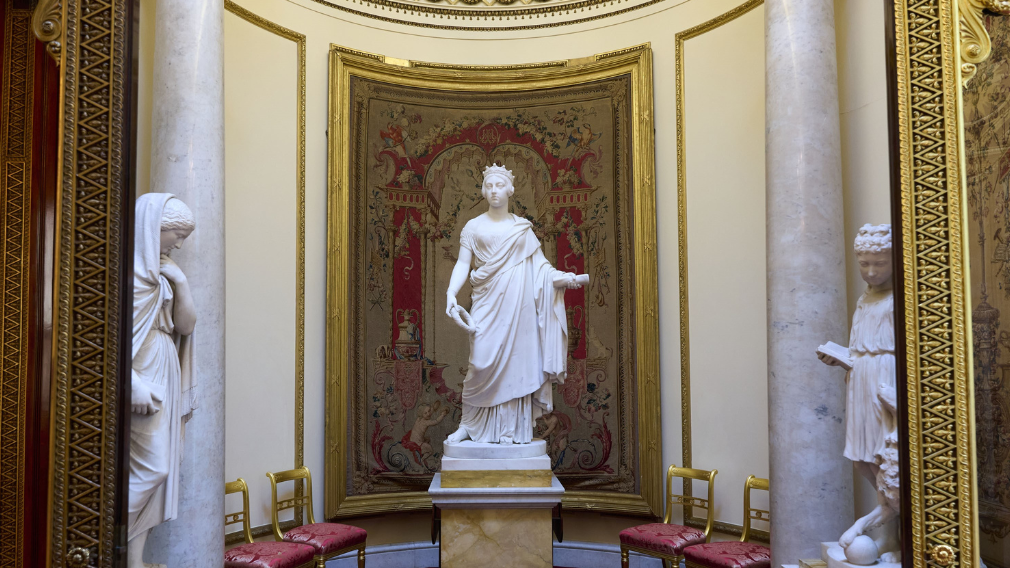 A full length marble statue of Queen Victoria in classical dress wearing coronet chased with dolphins.