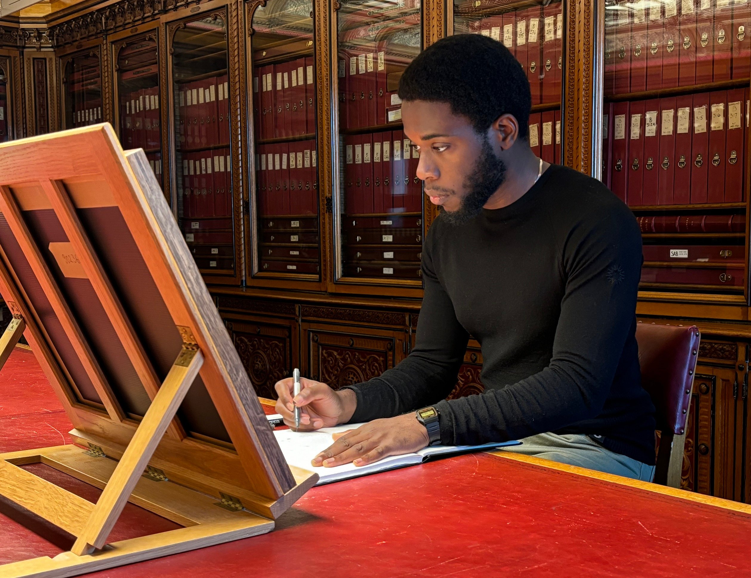 The artist Jesse Ajilore sits in front of a book stand sketching