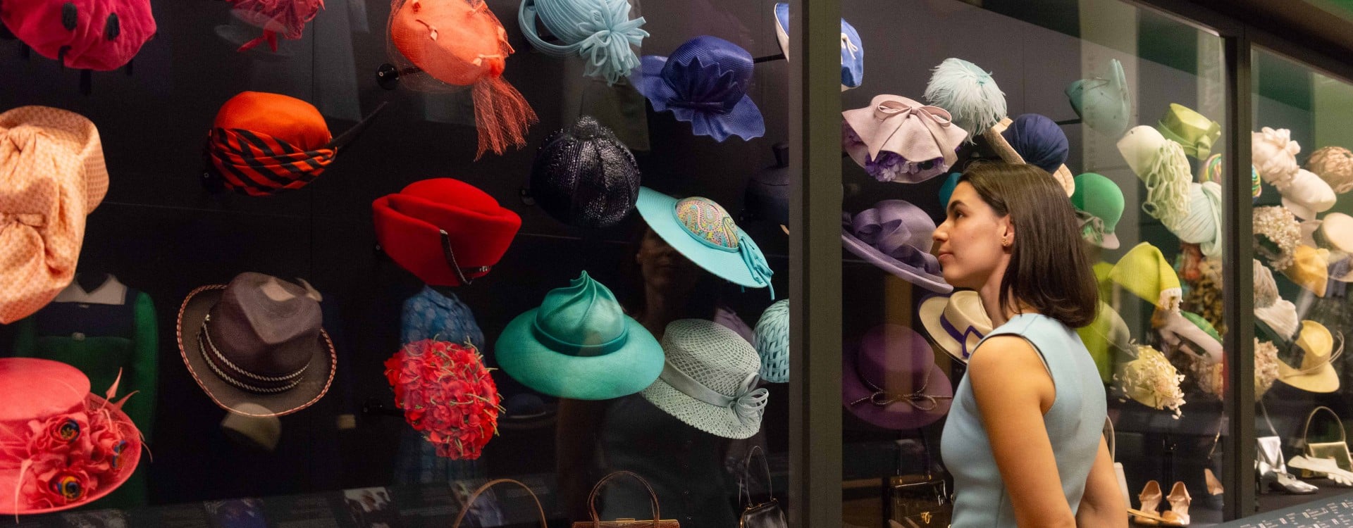 A visitor looks at a display of colourful hats in the exhibition Queen Elizabeth II: Her Life in Style