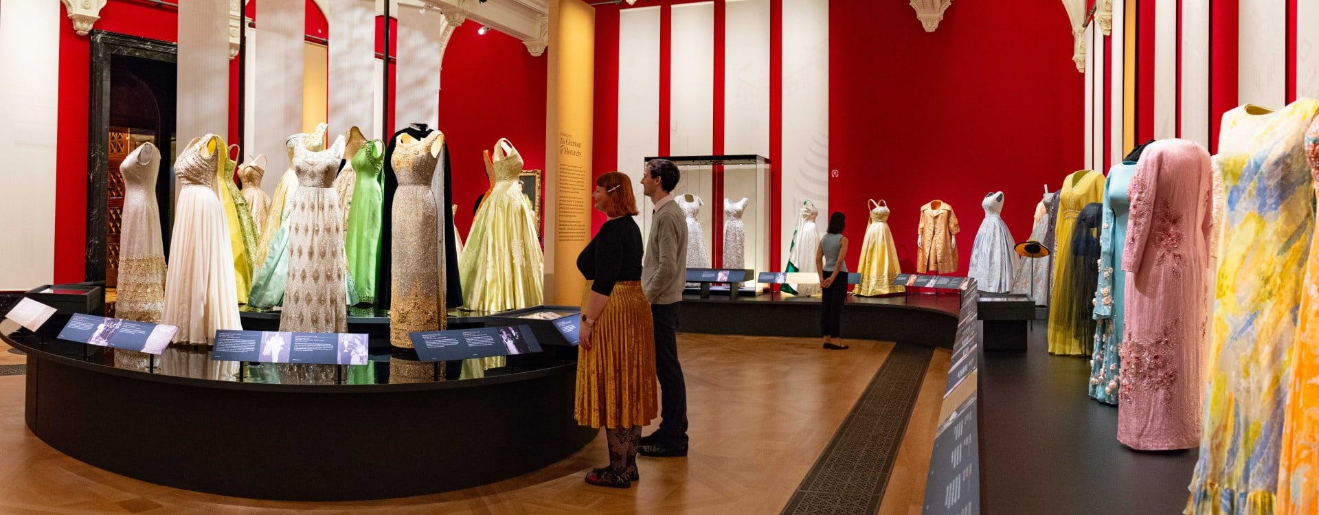 Visitors look at a display of colourful outfits in the exhibition Queen Elizabeth II: Her Life in Style