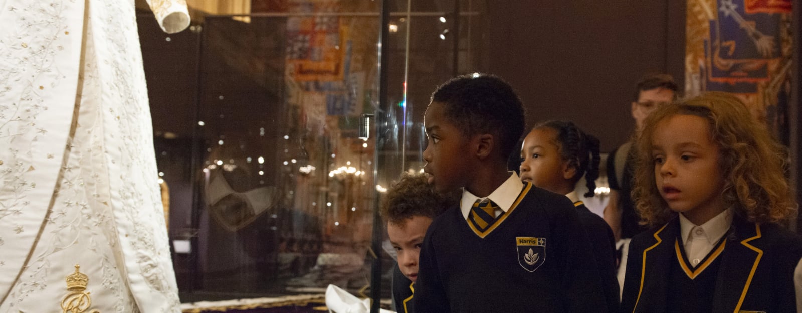 school children looking at glass cabinet displaying white dress