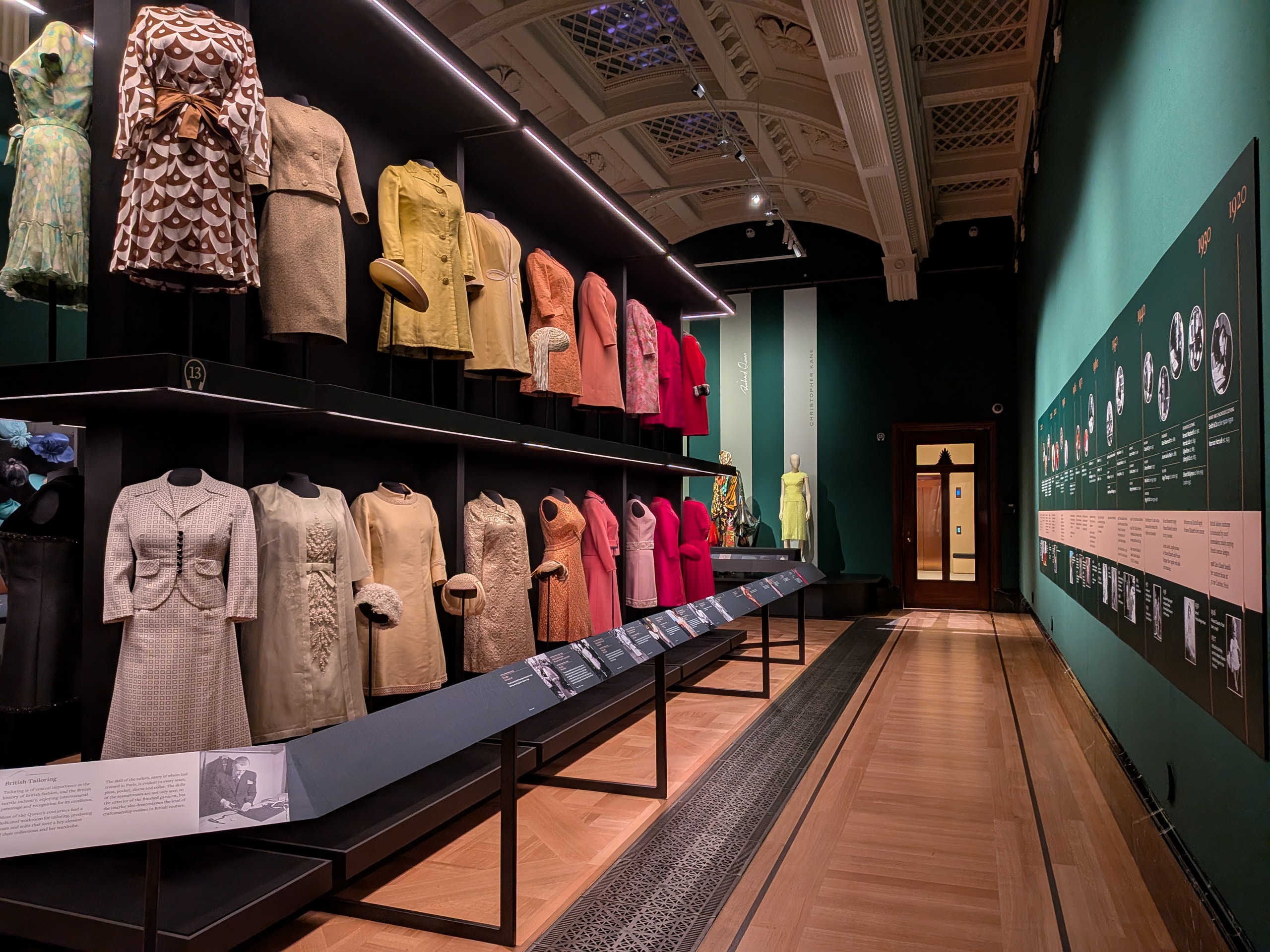 Photo of a gallery space with green walls and a display of colourful dresses