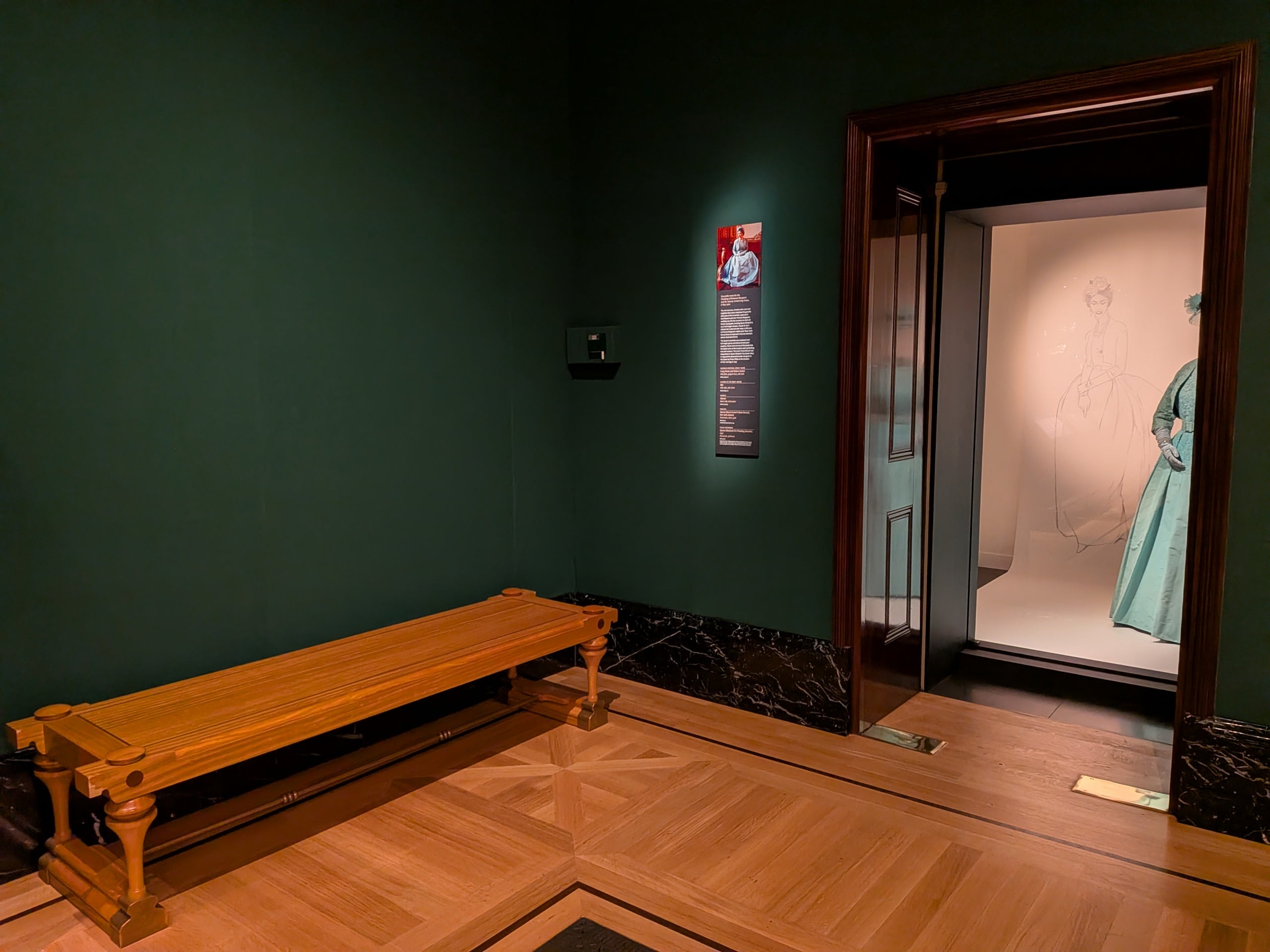 Photo of a gallery space with green wall and a wooden, backless bench.