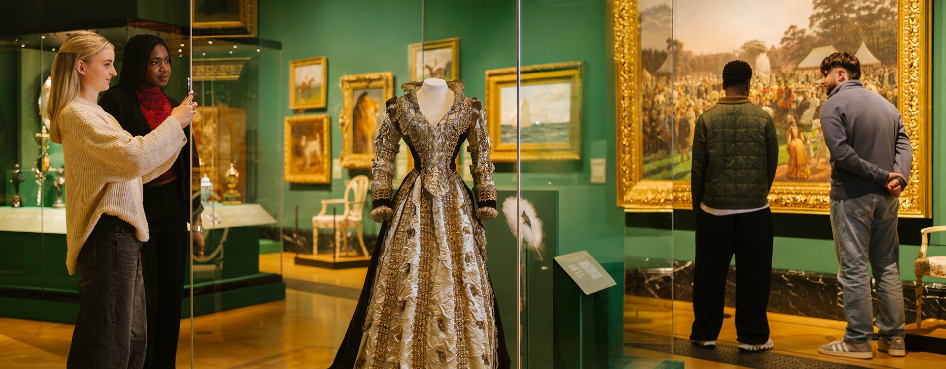 Visitors taking a picture of a dress in the exhibition 'The Edwardians: Age of Elegance'