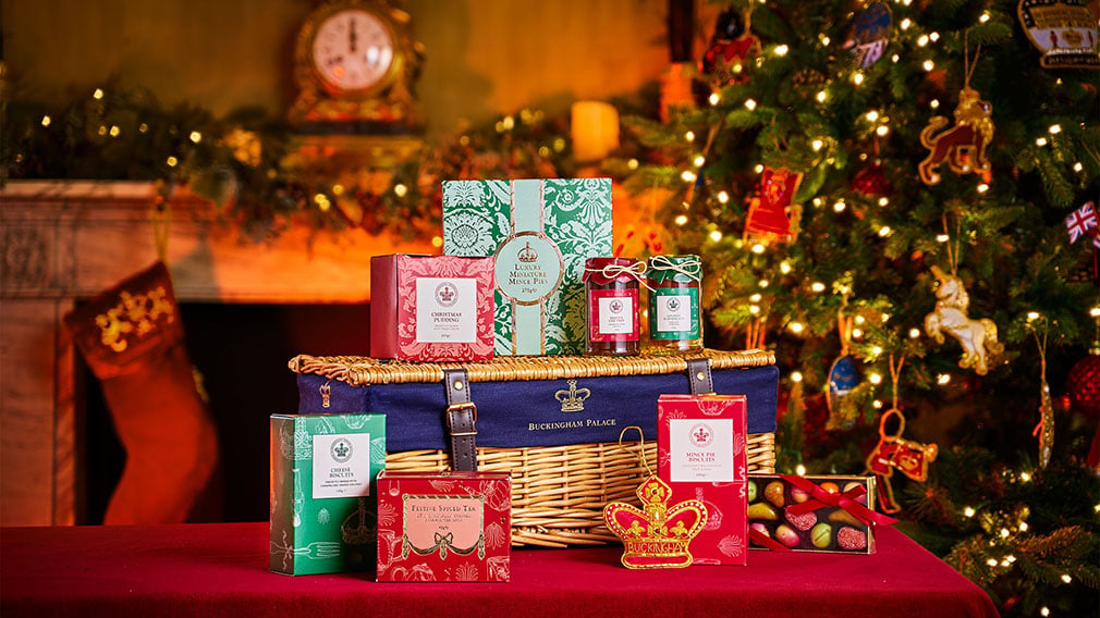 A table with a hamper and gifts from a shop. A Christmas tree and stocking is in the background.