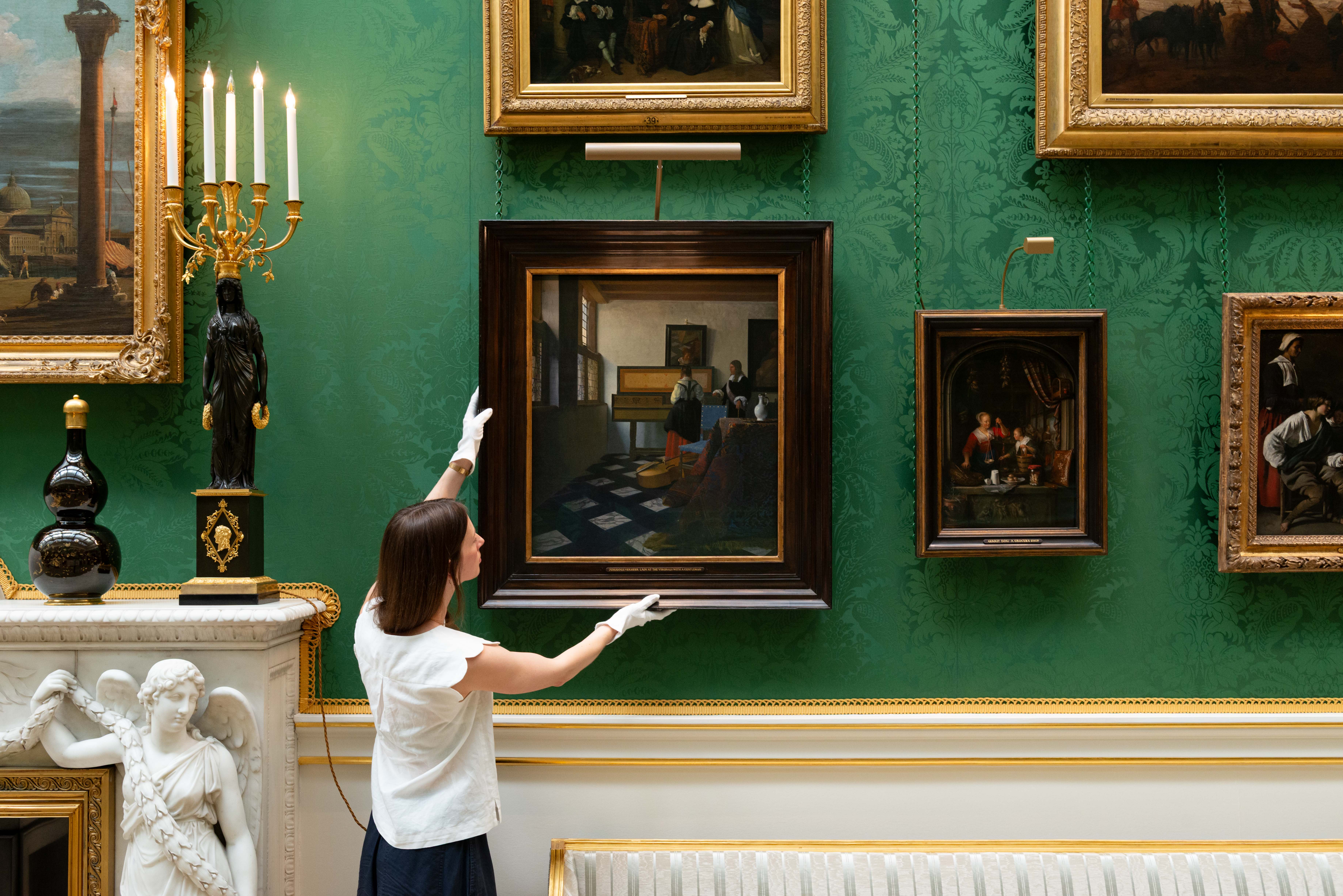 A curator making a final adjustment to Vermeer's painting known as The Music Lesson, which shows a man teaching a woman how to play an instrument