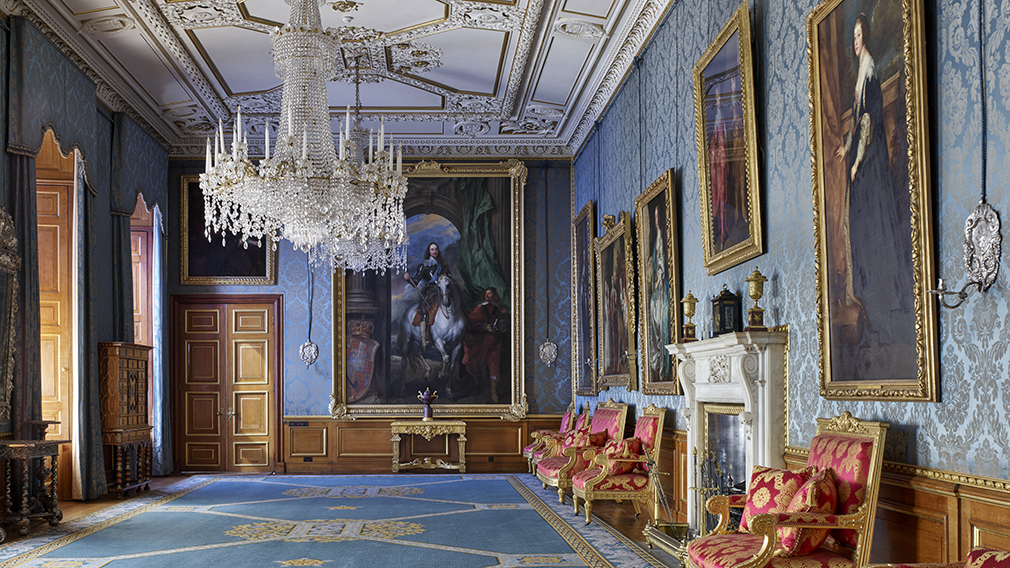 An ornate room filled with paintings and furniture. It has blue walls and carpet.