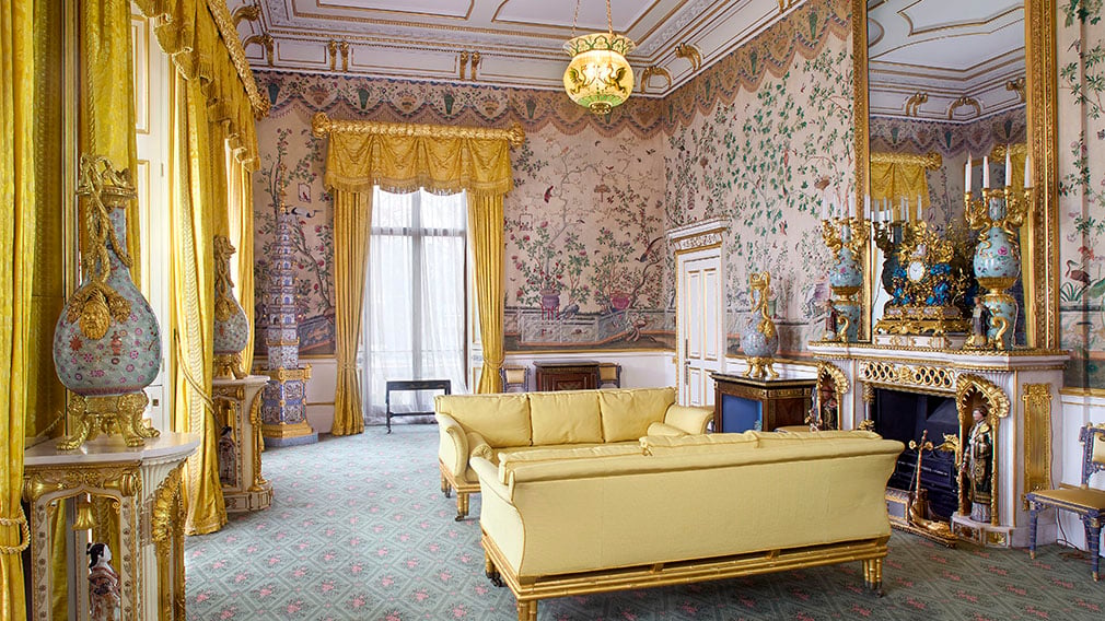 A ornately decorated room with yellow curtains and sofas.