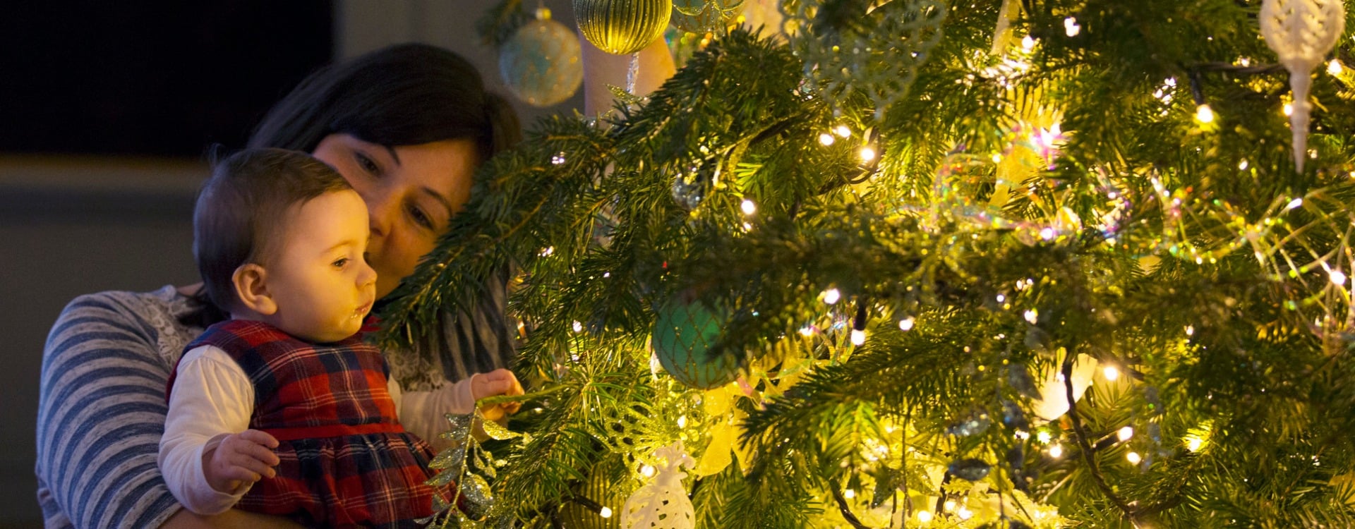 An adult and baby next to a Christmas tree