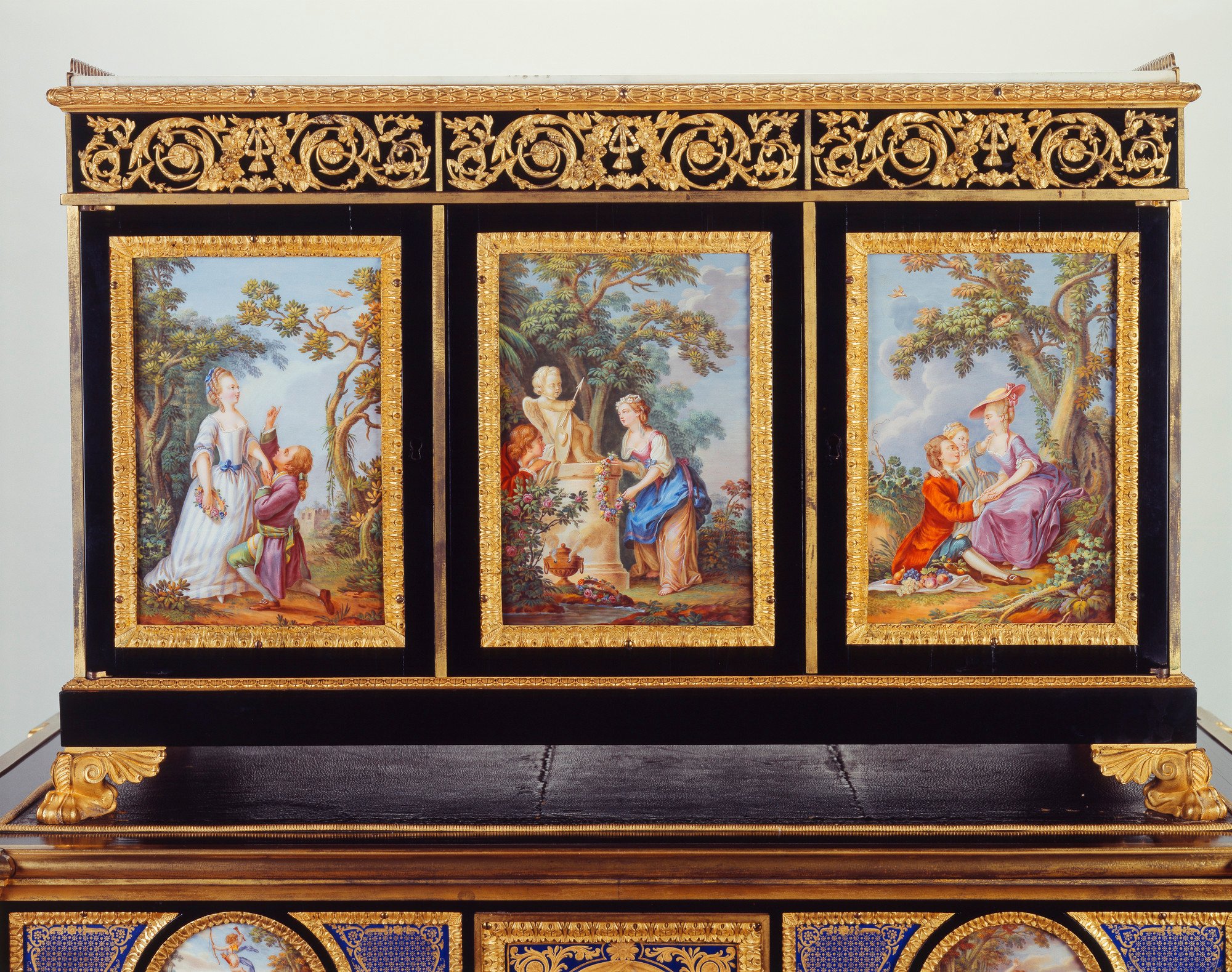 Rectangular porcelain-mounted cabinet on a similarly decorated table, inset with nineteen plaques, each with gilt metal border; cabinet with white marble top with pierced gilt metal gallery; on plinth base with gilt paw feet. Table with four fluted legs, 