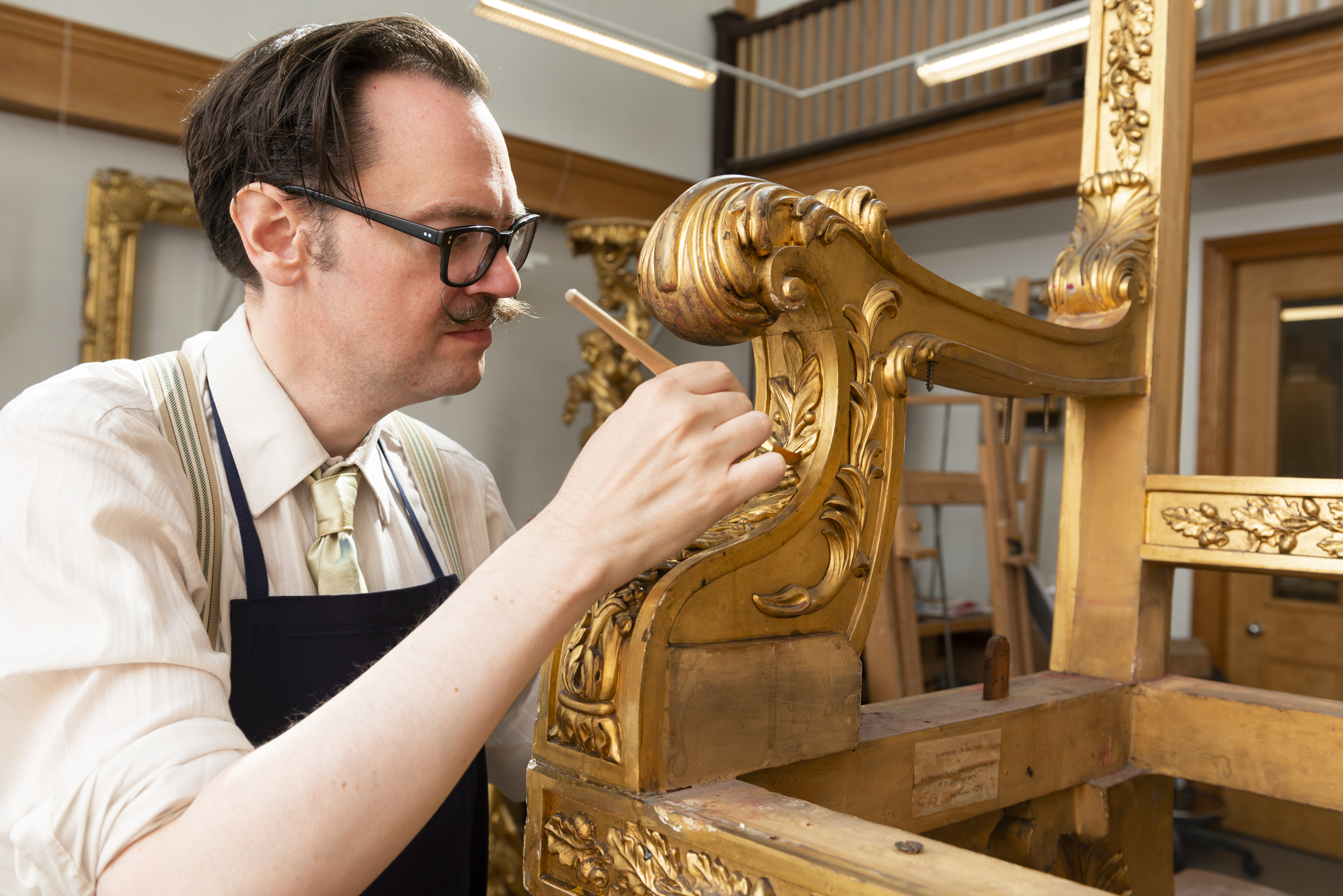 conservator working on gilt timber frame of throne