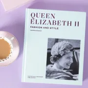 The book Queen Elizabeth II: Fashion and Style on a purple background, next to a cup of tea