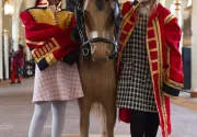 Two girls are wearing uniforms and standing next to a little wooden pony