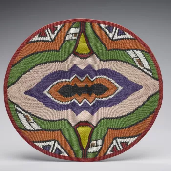 A colourful shallow basket or pot cover made of telephone wire (an imbenge).  
Traditional Zulu baskets were tightly woven from grasses and palm leaf. Today, craftspeople living in urban areas recreate many of the old patterns and forms with a new medium 