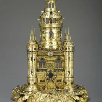 A silver-gilt table salt in the form of a tower with cylindrical corner turrets and a tall central turret with an open gallery and domed roof above, resting on a chased mound supported by dragons on ball feet, the salt is encrusted with jewels. The body o