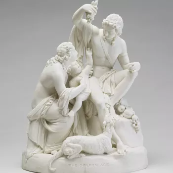 A Parian porcelain figure group; a woman seated to the left holding a child who reaches for a bunch of grapes held by a seated young man; wearing classical dress; set on rocky outcrop with flowers and fruit, a dog lying in foreground; oval base. 
Queen Vi