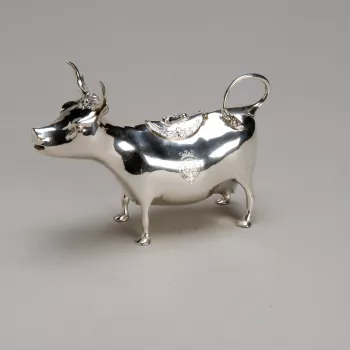 A continental silver cow creamer, w oval hinged lid, cast w foliate border. The body in the form of a long horned cow, the curved tail forming the handle & the mouth the spout. Side engrv w Edinburgh crest, garter & coronet.