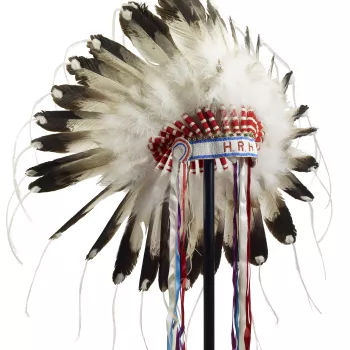 A First Nations feather headdress or war&nbsp;bonnet in Plains style, fitted with eagle (?) feathers threaded with white horsehair (?) at the tips and with blue, red, purple&nbsp;and white silk ribbons hanging from each side,&nbsp;and a blue&nbsp;and whit