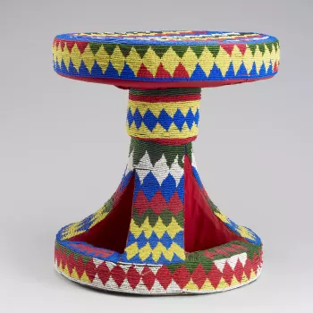 A stool with a circular seat and base covered all over with red, yellow, white and blue glass beadwork in a zig-zag pattern.
The size and decoration of Cameroon's ceremonial stools symbolise the status of the individual to whom the stool belongs. The empt