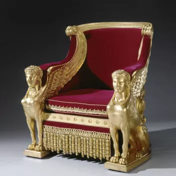 Pair of council chairs of carved and gilded pine and beechwood, covered in red velvet with gold trimmings and fitted with a cushion and valance. Backs shaped like Roman chariots, are solid to the ground and elaborately carved, as is the whole. Padded velv
