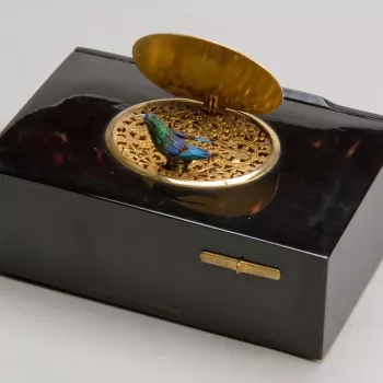 A rectangular tortoiseshell box, the lid mounted with a silver gilt oval hinged panel, chased and engraved with a pair of birds and flowers. The panel opens to reveal a blue and green feathered song bird which emerges from a pierced panel.