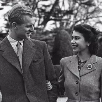 Photograph of a half length informal portrait of Princess Elizabeth (b. 1926), later HM Queen Elizabeth II standing on the right and HRH The Duke of Edinburgh (b. 1921) on the left. The couple face each other. Taken outside during their Honeymoon at Broad