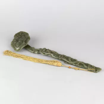 The ruyi sceptre with undulating shaft and turned-over head. The shaft carved in relief with a lingzhi spray, and the head with a bat; the bottom pierced for attaching the yellow silk tassel, with a spray of lily, the bloom hollowed to hold a gemstone, an