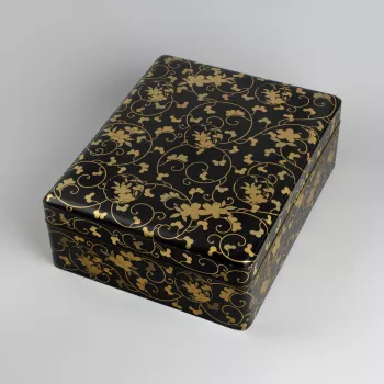 Rectangular box, with flanged rim to accommodate the cover, the top slightly domed and rounded at the edge and corners. Lacquered black, and painted over the top and sides in shades of gold, with a leafy vine scroll with superimposed prunus spray roundels