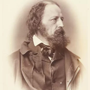 Photograph of the poet Alfred Tennyson facing three-quarters right. He wears an overcoat or cloak over a jacket with high lapels. He wears a pince-nez or eyeglass attached to a string around his neck. Half-length portrait. 