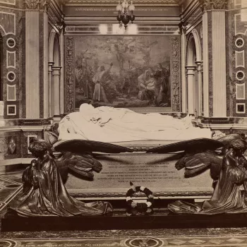Photograph of Prince Albert's tomb inside the Royal Mausoleum, Frogmore, in the Home Park, Windsor. The Prince's effigy is supported by winged angels and a single wreath lies against the side of the tomb. In the background, set against marble walls, porti