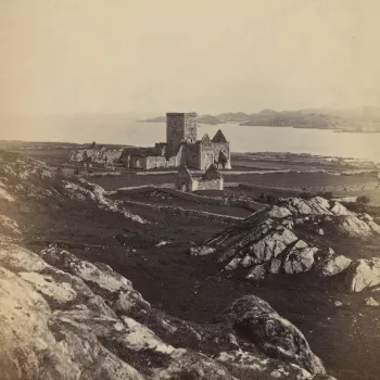 Photograph of the ruins of Iona Abbey situated on the Ross of Mull,&nbsp;a large peninsula on the Isle of Mull. In the foreground are large boulders. The central tower of the Abbey stands above the ruins of the nave and another ruined, smaller dwelling st