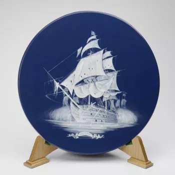 A Wedgwood circular ceramic plaque on blue ground with white slip image of the ship Victory at sea.
As part of the commemorations of the 200th anniversary of the Battle of Trafalgar, The Queen attended a banquet on board HMS Victory at Southampton. This p