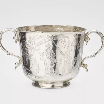 A silver two-handled cup on a shallow foot, with scroll handles, the body flat chased with chinoiserie scenes, showing one figure holding a parasol over another, exotic birds and plants. The reverse is engraved in Latin: Ex Regio Fulcro Regis Salus. 
The 