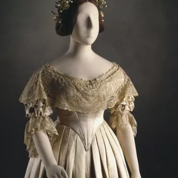 Wedding dress ensemble of cream silk satin; comprising pointed boned bodice lined with silk, elbow length gathered sleeves; deep lace flounces at neck and sleeves and plain untrimmed skirt en suite, gathered into waist with unpressed pleats. 
Although the