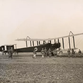 Photograph of Royal Flying Corps officers and airmen standing around a plane. In the cockpit of the plane sits Prince Albert, later King George VI (1895-1952). Photograph taken in Hendon.