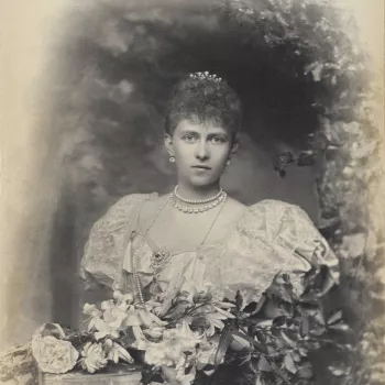 Photograph of a head and shoulder length portrait of Queen Sophia of Prussia (1870-1932) facing the camera, her body slightly angled to the left. She is&nbsp;framed by an arched structure featuring various fauna and&nbsp;poses in front of a flower arrange