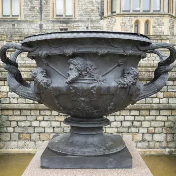 A bronze replica of the Warwick Vase, handles intertwined, fluted and leaf capped. The body with vine leaves and berries, scrolls and female and male heads in high relief. The base and top rim beaded and with tongue border. On rectangular speckled granite