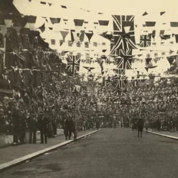 Black and white photo showing a street decorated with large amounts of flags and bunting