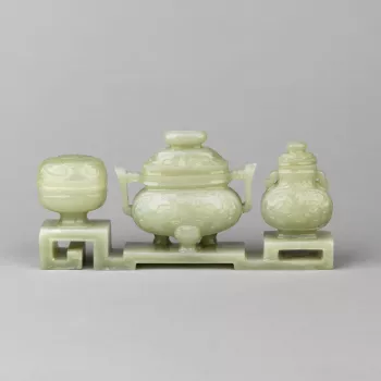 Three vases in archaic bronze forms carved on a stepped stand: in the centre, an incense burner, with upright handles and three animal-style feet, carved with a taotie, the domed cover with an oval button knob; to one side, a two-handled vase, also with t