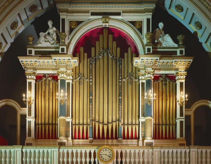 Three manual organ with a maplewood console in a painted and gilded case in the form of a triumphal arch flanked by life-size seated plaster figures and two gilded roundels of Handel.In 1818 Lincoln had installed an organ in Nash's newly built Music Room 