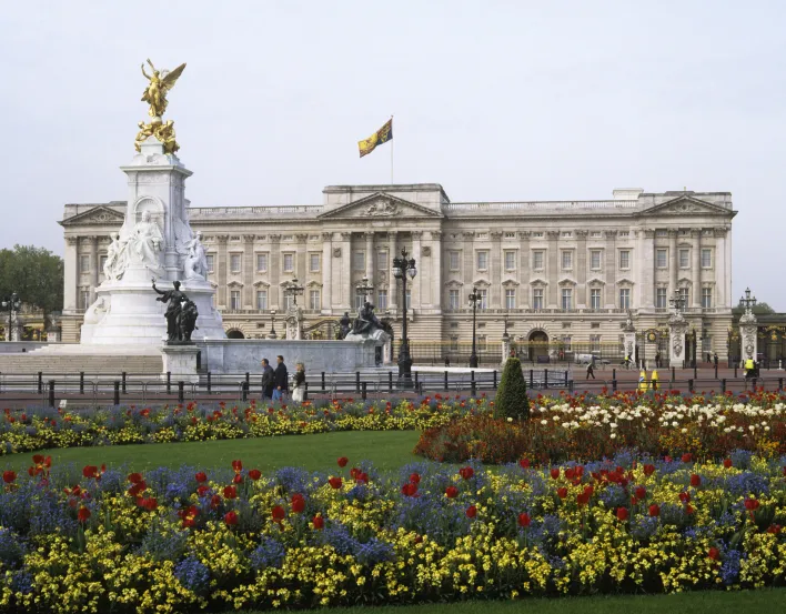 The grey stone facade of Buckingham Palace with gates and flower beds