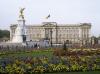The grey stone facade of Buckingham Palace with gates and flower beds