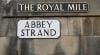 A image of a brick wall with a street sign with the text 'The Royal Mile' and another sign with the text 'Abbey Strand'.