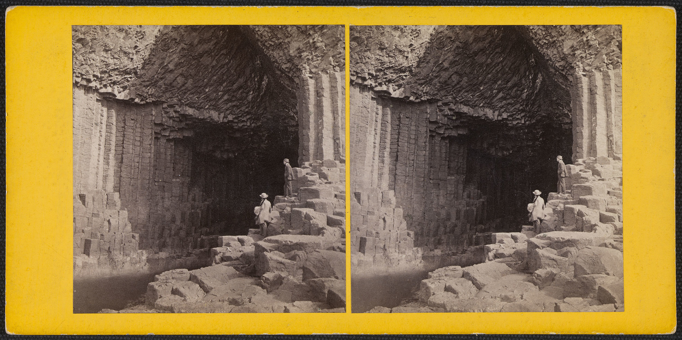Stereoscopic photograph of the entrance to Fingal's Cave, Staffa in the Inner Hebrides in Scotland. Standing on the right of the cave entrance are two men; one with his back to the viewer and another who stands in left side profile. 
Like the Giant's Caus